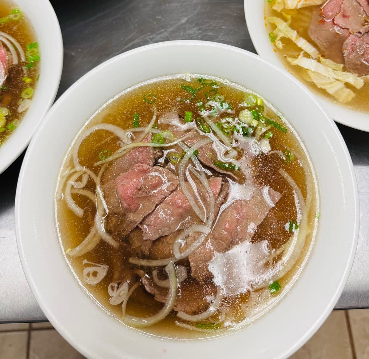 A bowl of rare beef phở with onions and herbs.